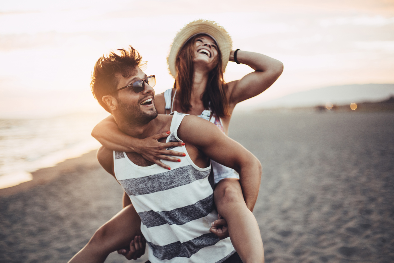 Lighthouse family therapy - home page a couple at a beach laughing while the man is piggybacking the lady with a hat